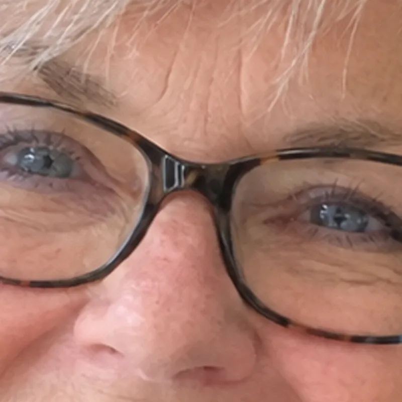 Detail of a woman's eyes and tortoiseshell glasses from a small photograph, stretched to print size the ordinary way: the frames, lashes and hair are blurred.